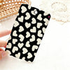 A black card holder featuring a pattern of white heart shapes, resting on a white surface next to a woven basket.