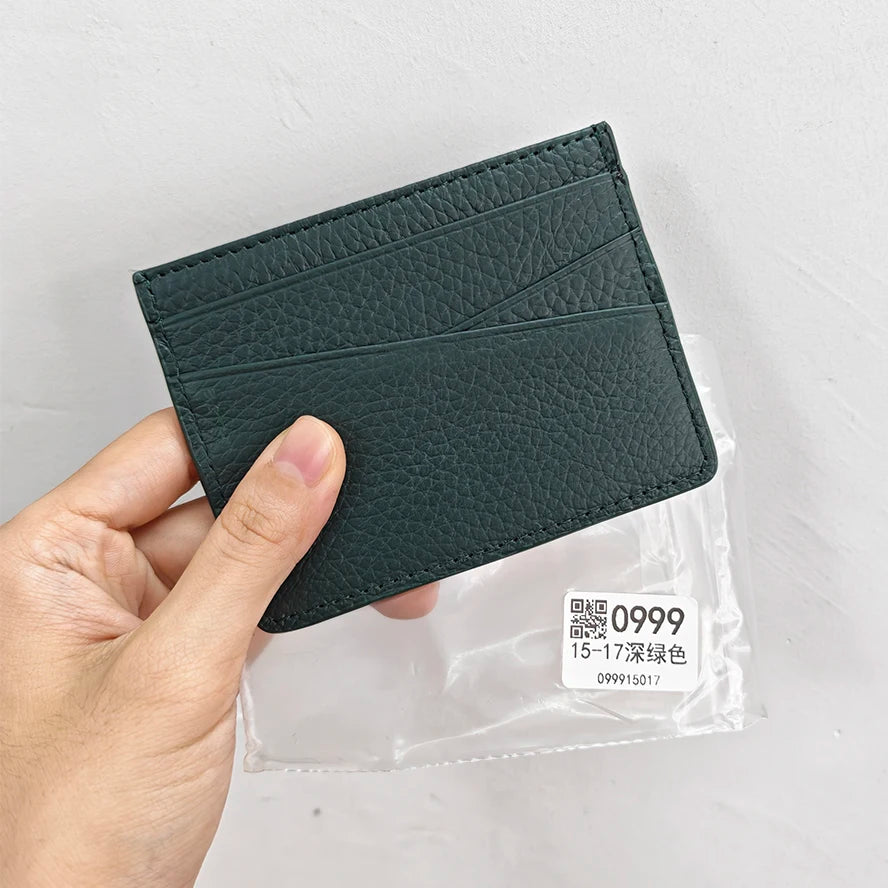 Une main tient un porte-cartes en cuir vert foncé et gravé, avec une pochette en plastique transparent.