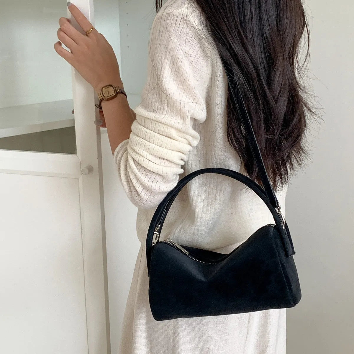 A woman holds a black faux suede crossbody bag against a white background.