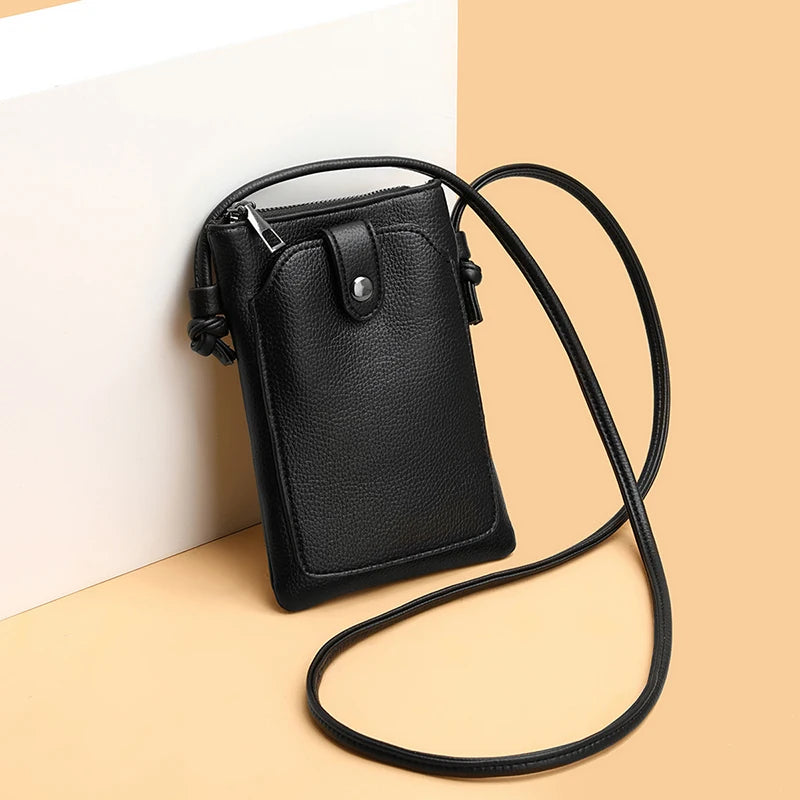 A black compact PU leather crossbody bag resting on a light beige surface.