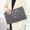 A woman holds a gray laptop sleeve with a purple strap and gold hardware against a white background.