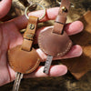 A hand holds a genuine leather key fob cover with a keychain ring and attached key.