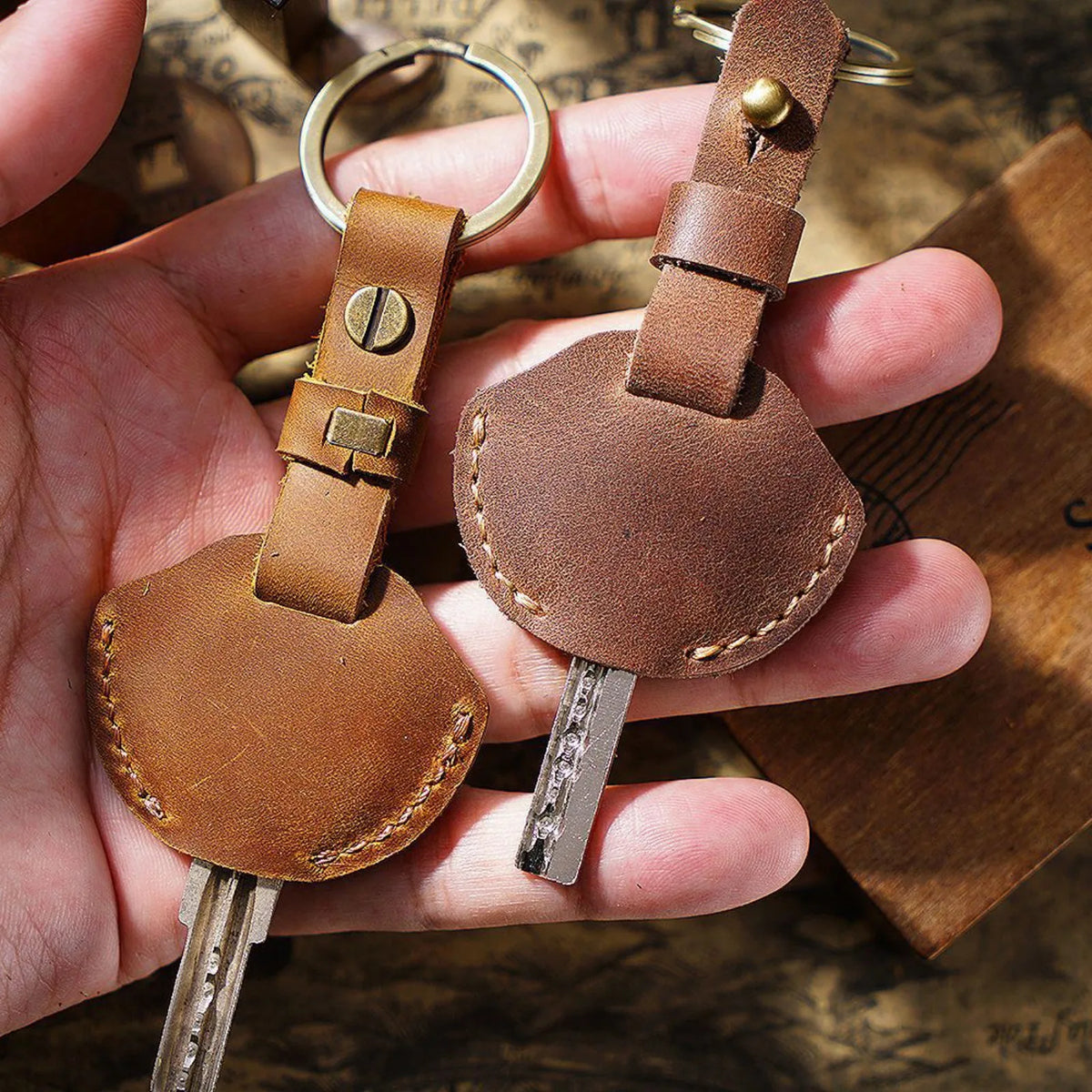 A hand holds a genuine leather key fob cover with a keychain ring and attached key.