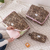 A hand is opening a leopard print travel makeup organizer bag, revealing pink tissue paper inside.