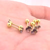 A set of gold-toned stainless steel ear stud earrings featuring purple gemstone accents displayed on a hand.