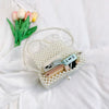 A handmade pearl beaded clutch bag with a strap resting on white fabric next to a bouquet of tulips.