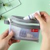 A hand holds a clear double-layer zippered pouch with a gray mesh exterior and a white tube inside.