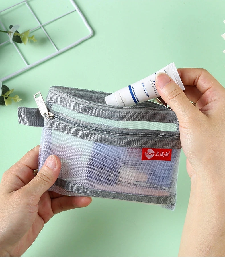 A hand holds a clear double-layer zippered pouch with a gray mesh exterior and a white tube inside.