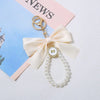 Llavero decorativo con hebilla dorada, dije de corbata y una cadena de perlas blancas.