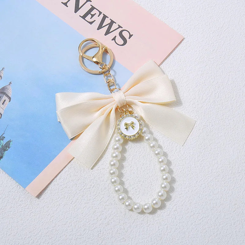 Llavero decorativo con hebilla dorada, dije de corbata y una cadena de perlas blancas.
