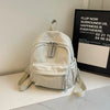 A light beige lightweight corduroy daily backpack is displayed on a white surface next to a framed sign.