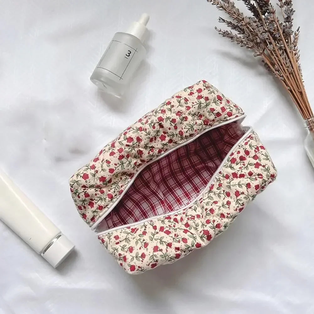 Bolsa de maquillaje acolchada con cremallera floral y forro a cuadros, con una botella blanca cercana.