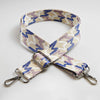A beige and purple patterned jacquard strap for an adjustable wide crossbody bag.