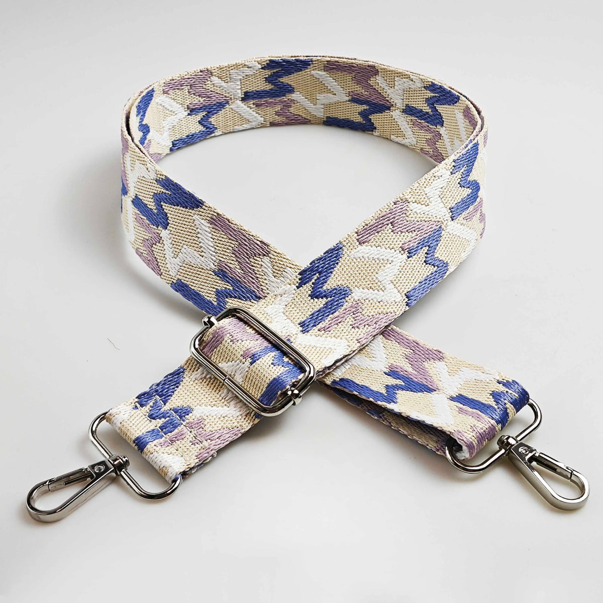A beige and purple patterned jacquard strap for an adjustable wide crossbody bag.
