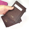 A hand holds a dark brown genuine leather zipper card holder and coin purse.