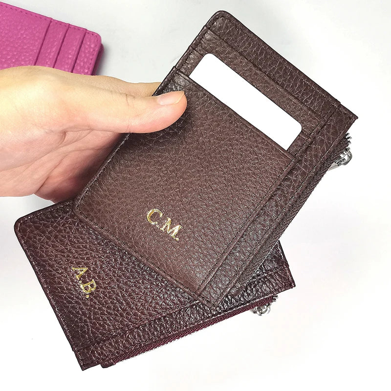 A hand holds a dark brown genuine leather zipper card holder and coin purse.