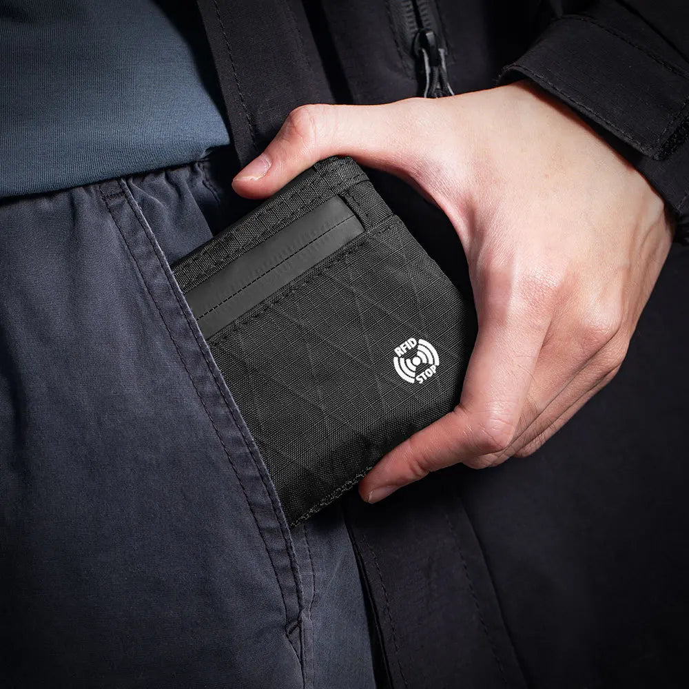A hand is holding a black RFID blocking travel wallet with a carabiner attached, visible inside a dark garment pocket.