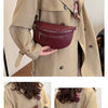 A woman models a maroon PU leather multi-pocket crossbody bag with a striped strap against a beige coat.
