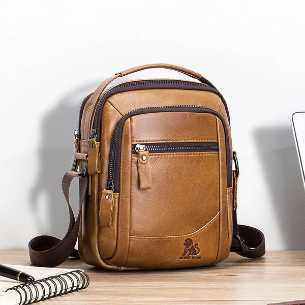 A brown genuine leather cowhide crossbody bag with a tan trim and dark brown strap resting on a wooden surface.