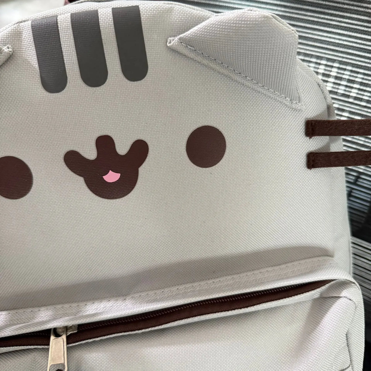 A white canvas backpack featuring a cute Pusheen cat face design with dark brown markings and eyes.