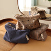 Une pile de pochettes de rangement cosmétiques à rayures marron et marine sur une surface en bois.