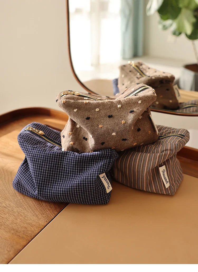 Une pile de pochettes de rangement cosmétiques à rayures marron et marine sur une surface en bois.