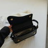 Bolso cruz de cuero negro vintage con solapa y compartimento con cremallera sobre una superficie blanca.