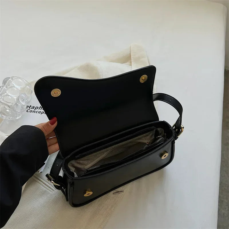 Bolso cruz de cuero negro vintage con solapa y compartimento con cremallera sobre una superficie blanca.
