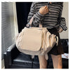 A woman holds a beige nylon shoulder bag with a patterned strap in an indoor setting.