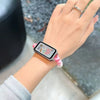 A hand wearing a smartwatch with a pink elastic strap on a light gray sleeve.
