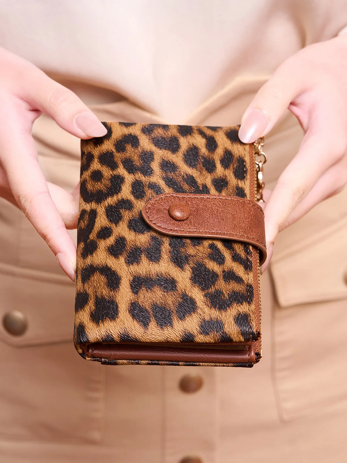 A close-up of a brown vintage leopard print women's wallet being held by hands against a beige blazer.