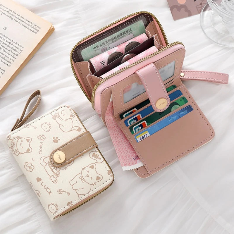 A pink and beige cat cartoon coin purse and card holder wallet with a zipper closure resting on a white surface.