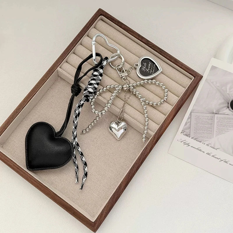 A set of black leather and silver bow keychains displayed in a wooden box.