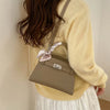 A woman wearing a yellow sweater and white skirt holds an elegant taupe PU leather crossbody clutch bag.