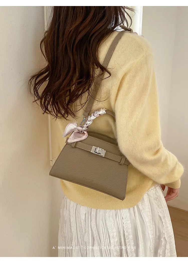A woman wearing a yellow sweater and white skirt holds an elegant taupe PU leather crossbody clutch bag.