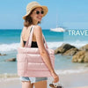 A woman wearing a pink quilted puffer tote bag stands on a beach with the ocean in the background.