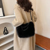 A woman is holding a beige coat and a black faux fur tote bag with a thin strap.