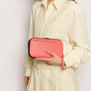 A woman wearing a cream collared shirt holds a pink passport organizer.