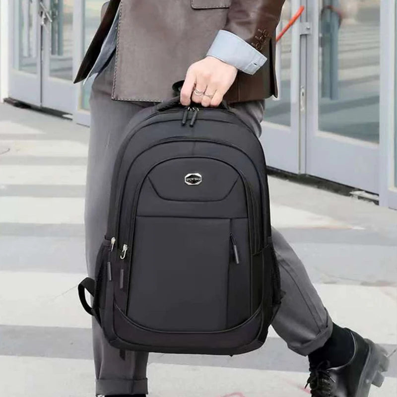A person is carrying a black unisex double-shoulder travel backpack while walking outdoors.