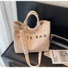 Sac à épaule beige côtelé avec une sangle en cuir, exposé sur une surface sombre à côté d'un ordinateur portable.