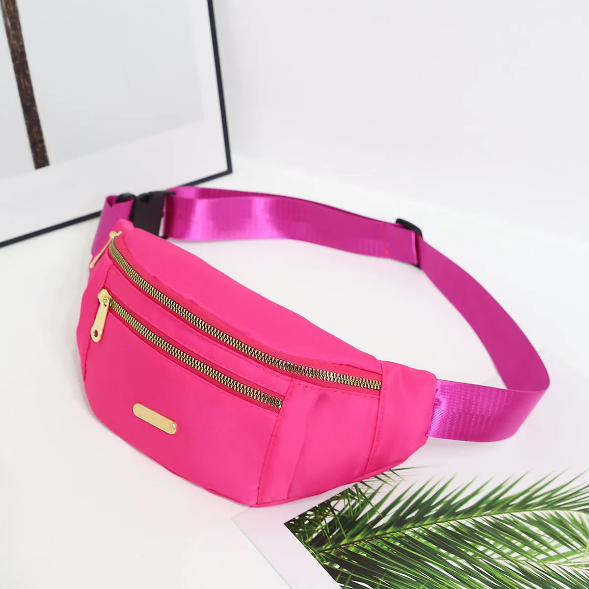 A bright pink lightweight nylon crossbody fanny pack with a gold zipper and a black strap, resting on a white surface.