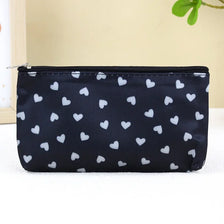 Black cosmetic bag with a white heart pattern and a silver zipper on a white surface.