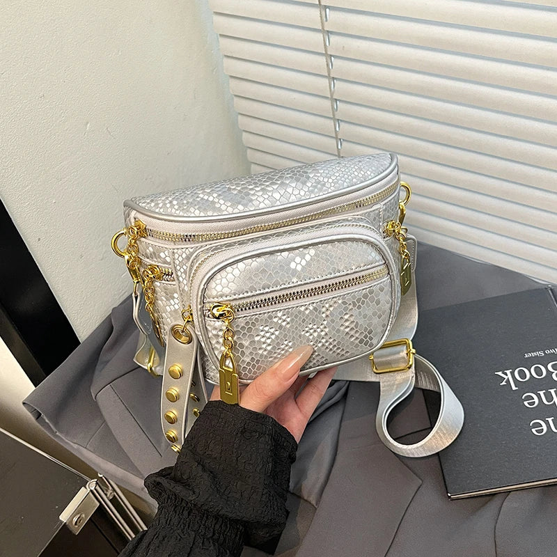A hand holds a silver textured Rivet Waist Bag crossbody bag against a gray background.