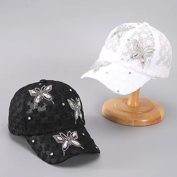 Casquette de baseball noire en maille avec broderie florale argentée, à côté d'une version blanche sur une planche de bois