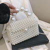 A handmade pearl beaded clutch bag with a strap resting on a dark book, next to a hand showing several pearls.