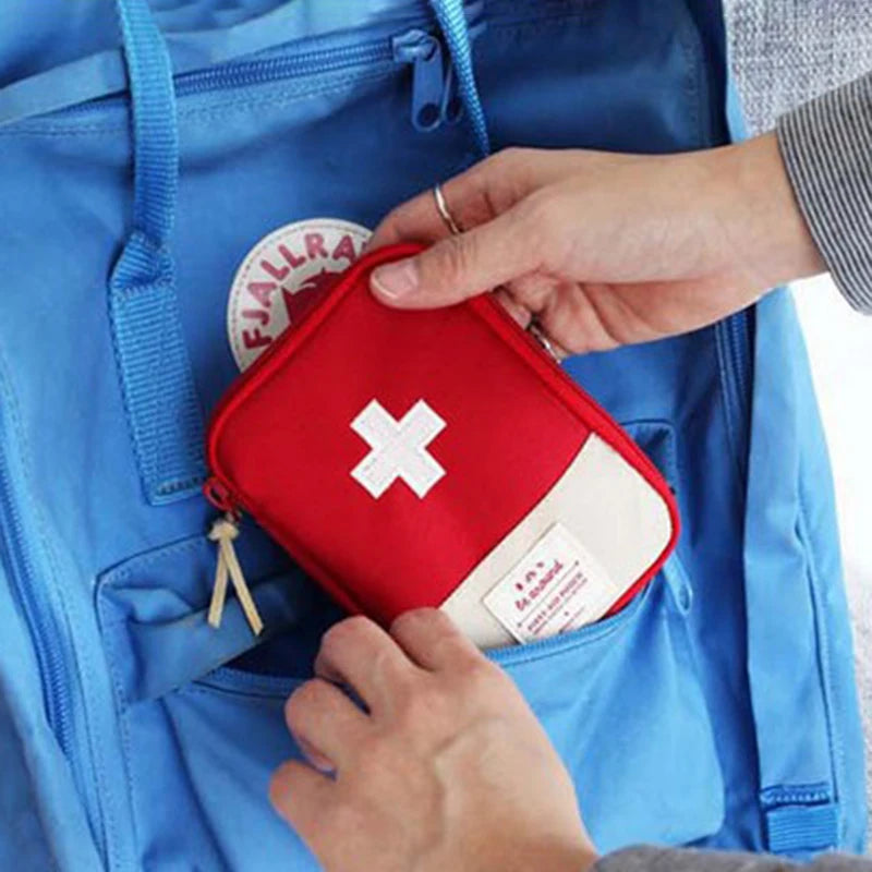 A hand is placing a red compact survival and first aid kit into a blue backpack pocket.