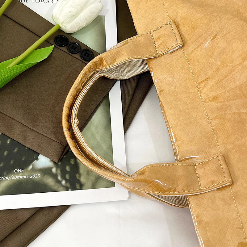 Primer plano de un bolso tote de PVC color canela con ribete de cuero beige claro y una flor de tulipán blanca descansando so