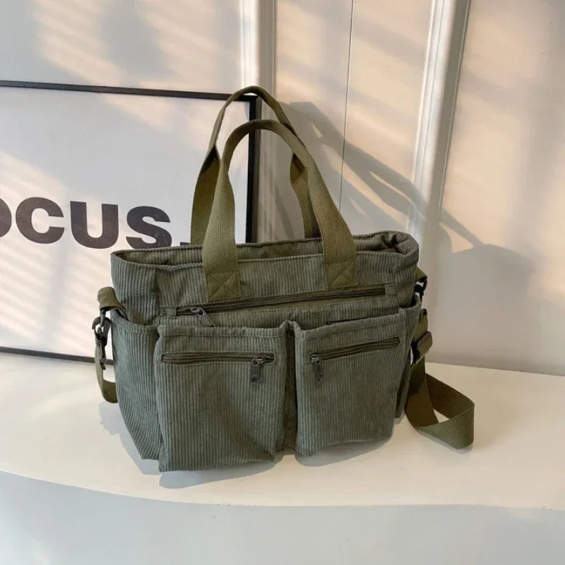 A olive green textured corduroy tote bag with adjustable straps resting on a white surface.