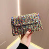 A hand holds a rectangular luxury rhinestone evening clutch bag decorated with colorful jewels and sequins.