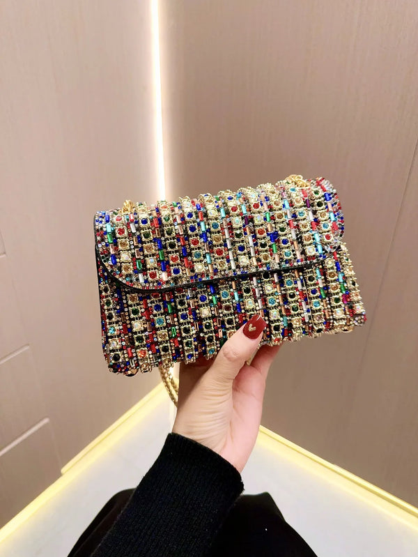 A hand holds an elegant rhinestone leather evening clutch bag sparkling with colorful stones.